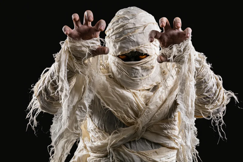 Mummy in white bandages with glowing eyes reaching forward against black background