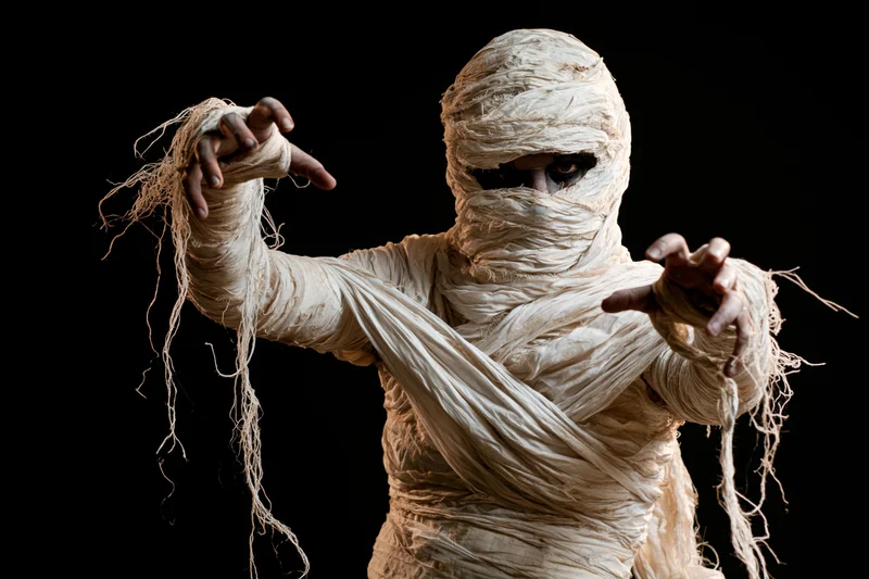 Mummy in white bandages with arms raised against black background