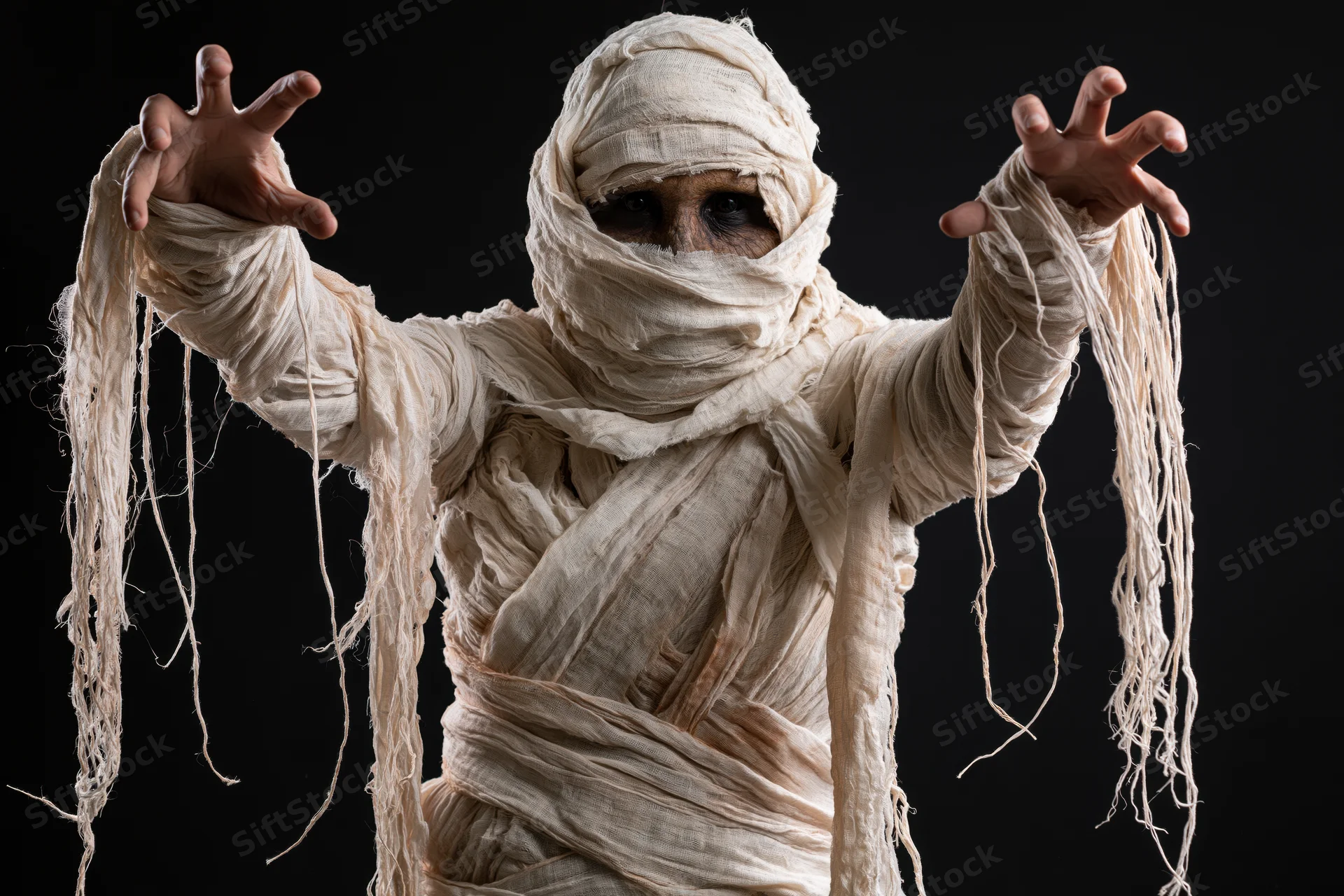 Mummy in diy costume with arms raised and claws extended against black background
