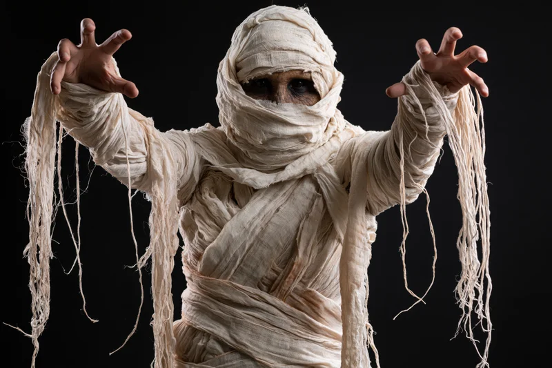 Mummy in diy costume with arms raised and claws extended against black background