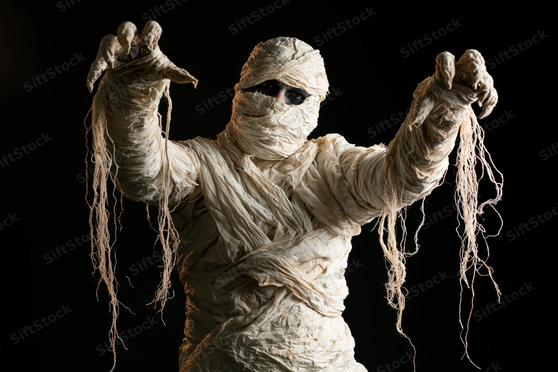Person in mummy costume with arms raised and clawed hands against black background