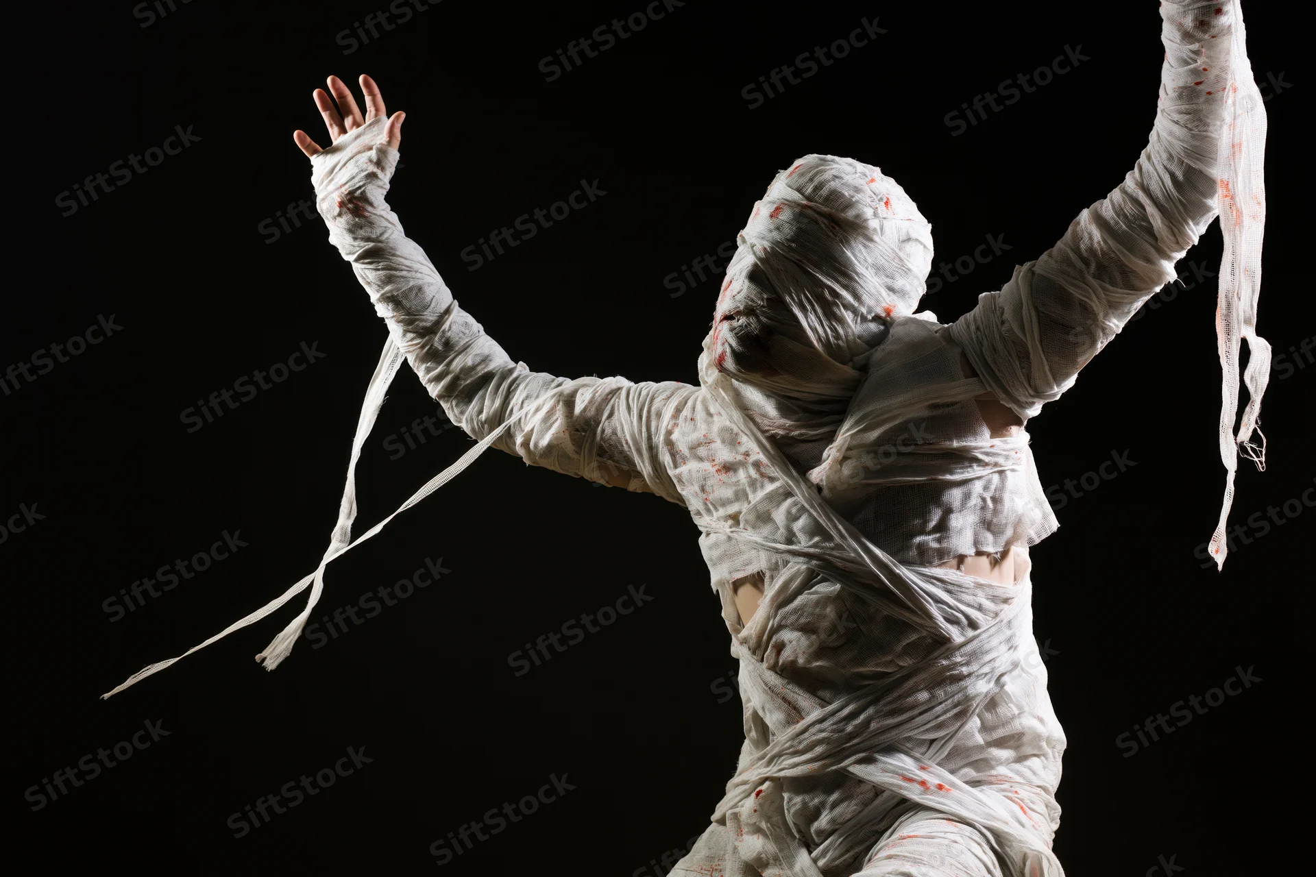 Mummy in white bandages with arms raised against black background