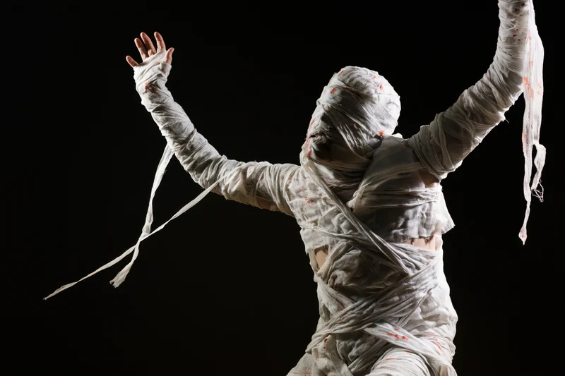 Mummy in white bandages with arms raised against black background