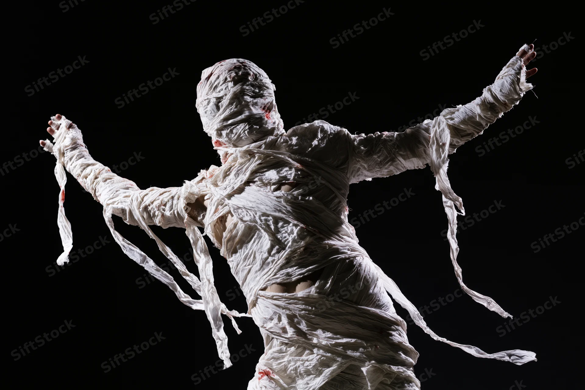 Mummy in white bandages with arms outstretched against black background