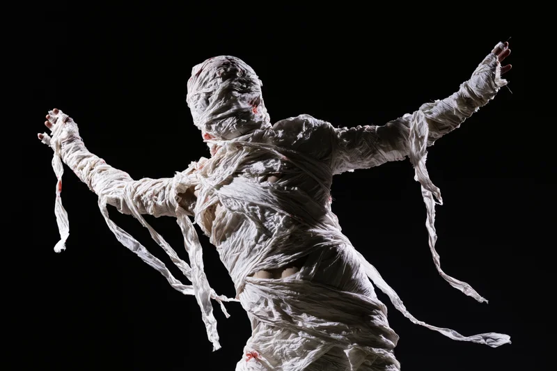 Mummy in white bandages with arms outstretched against black background