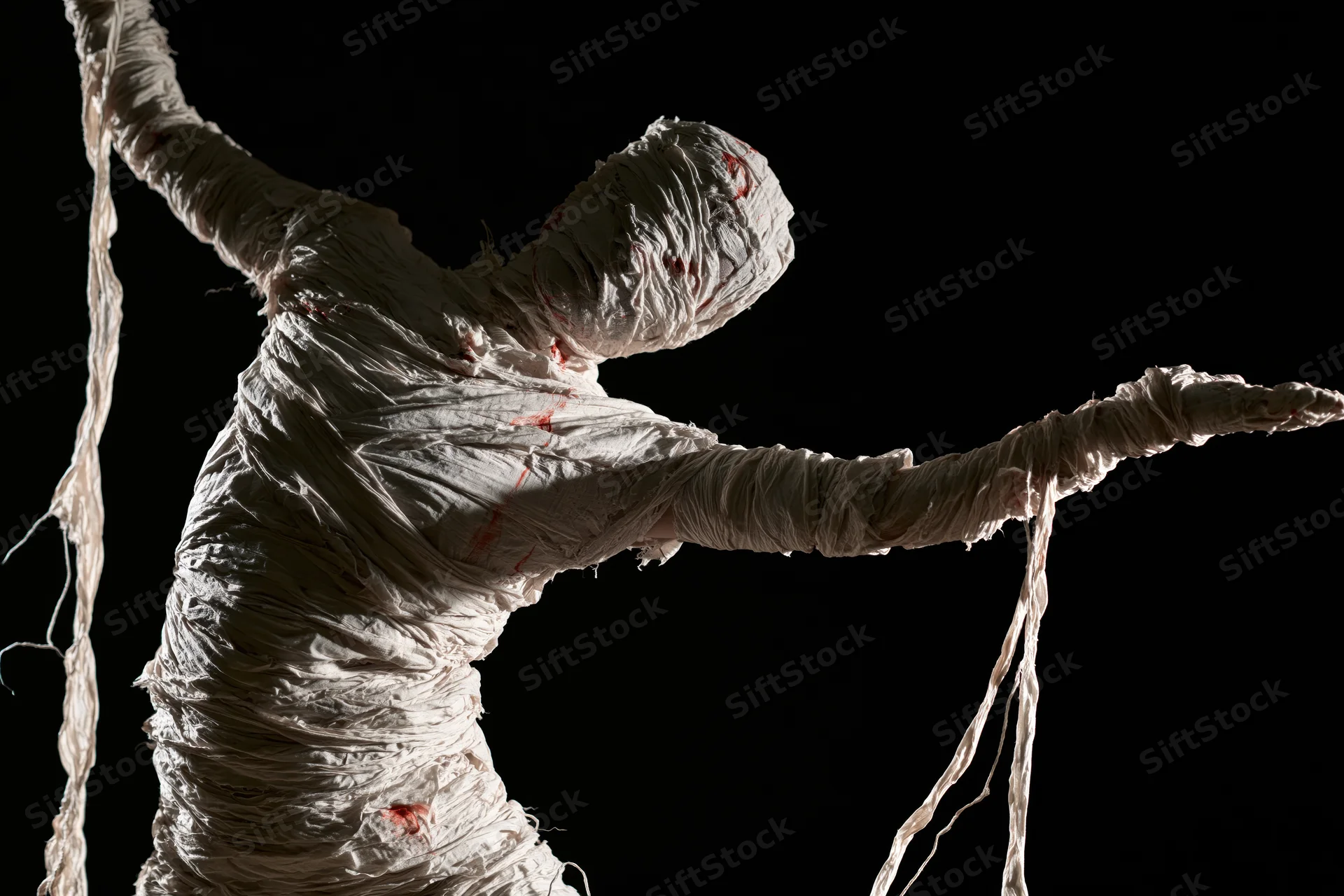 Mummy figure wrapped in bandages with arms outstretched against black background