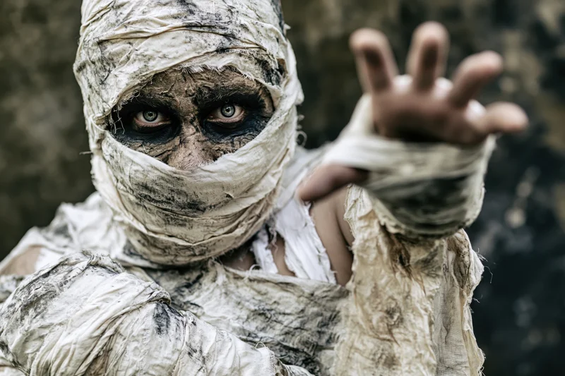 Mummy in elaborate costume with bandages reaching forward in closeup portrait