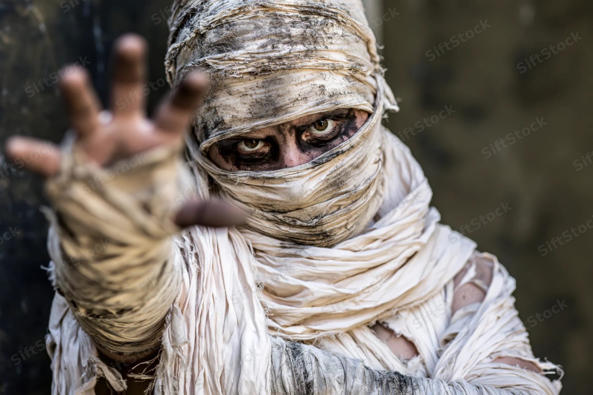 Mummy in elaborate costume with bandages wrapped around face and hand raised in gesture