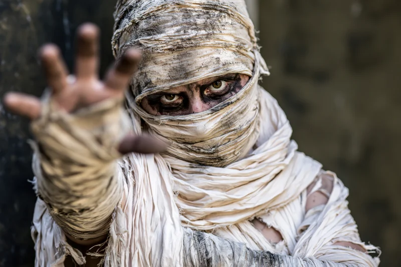 Mummy in elaborate costume with bandages wrapped around face and hand raised in gesture