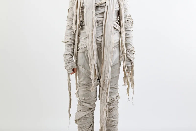 Person in full-body mummy costume wrapped in bandages standing upright against white background
