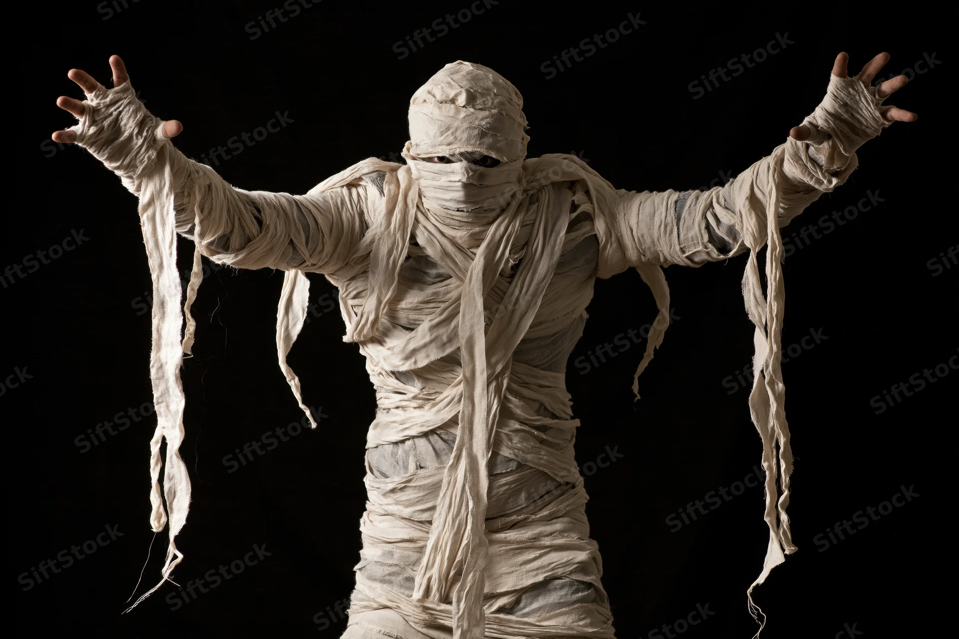 Mummy in full costume with arms raised and hands visible against black background