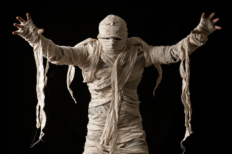 Mummy in full costume with arms raised and hands visible against black background