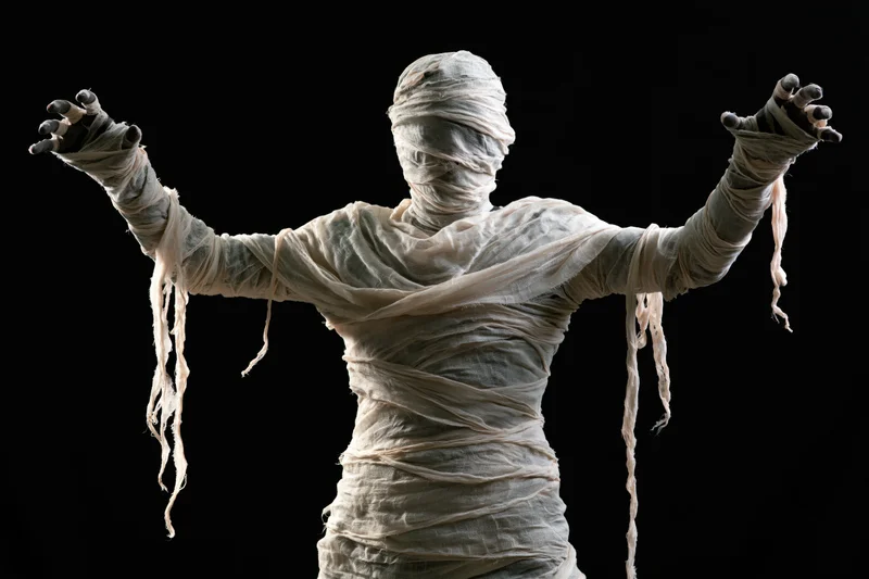 Mummy in full costume with arms raised and hands visible against black background