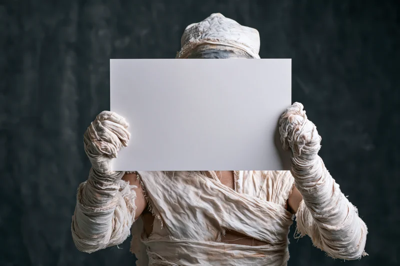Mummy in full bandage costume holding blank white sign against dark textured background