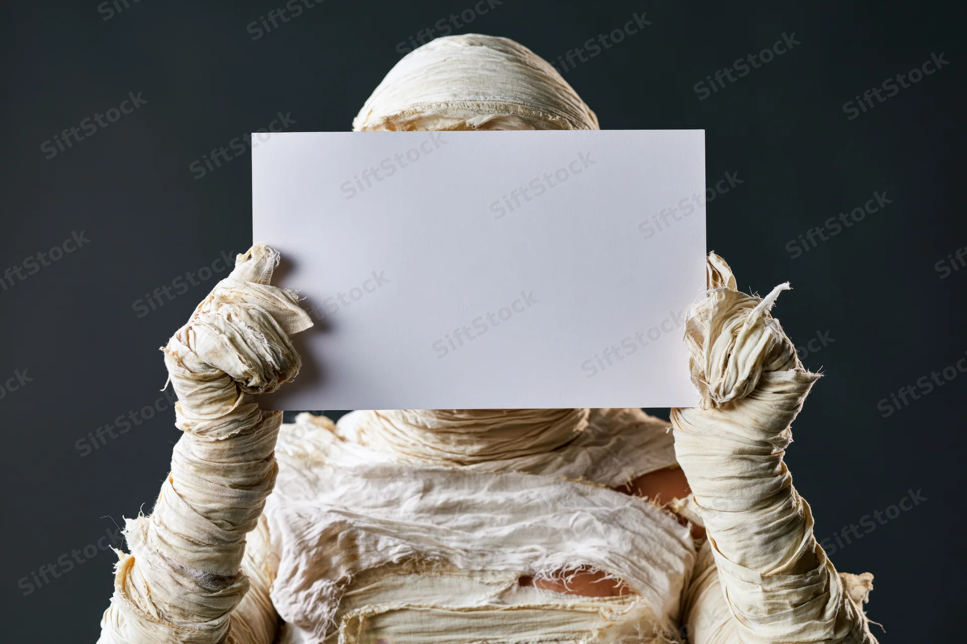 Mummy in full bandage costume holding blank white paper in front of face