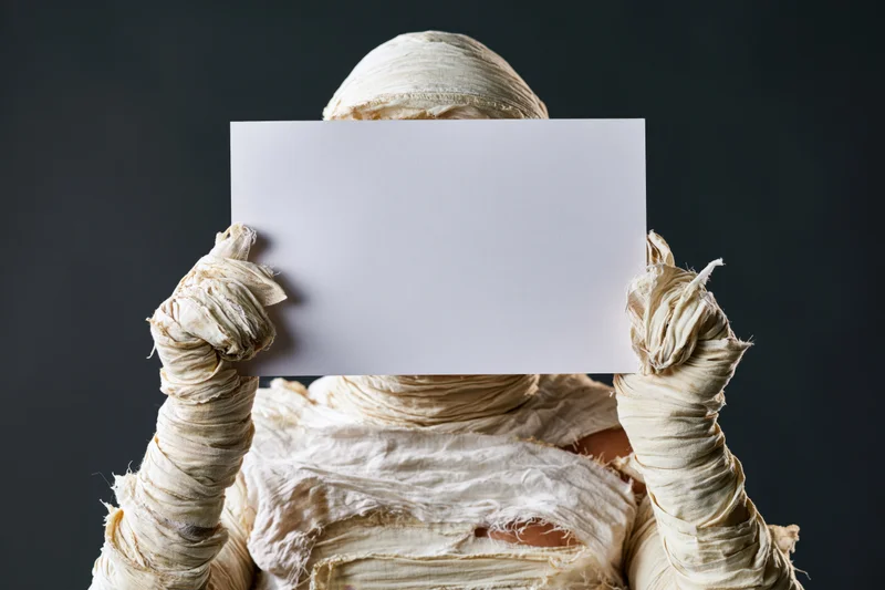 Mummy in full bandage costume holding blank white paper in front of face