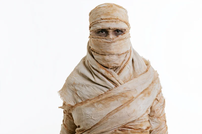 Person in full mummy costume wrapped in bandages standing upright against white background