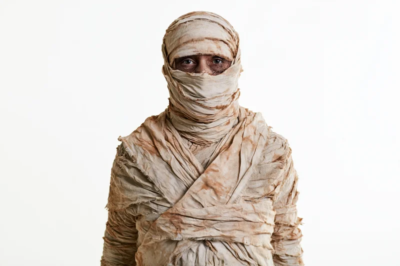 Person in full mummy costume wrapped in bandages standing upright against white background