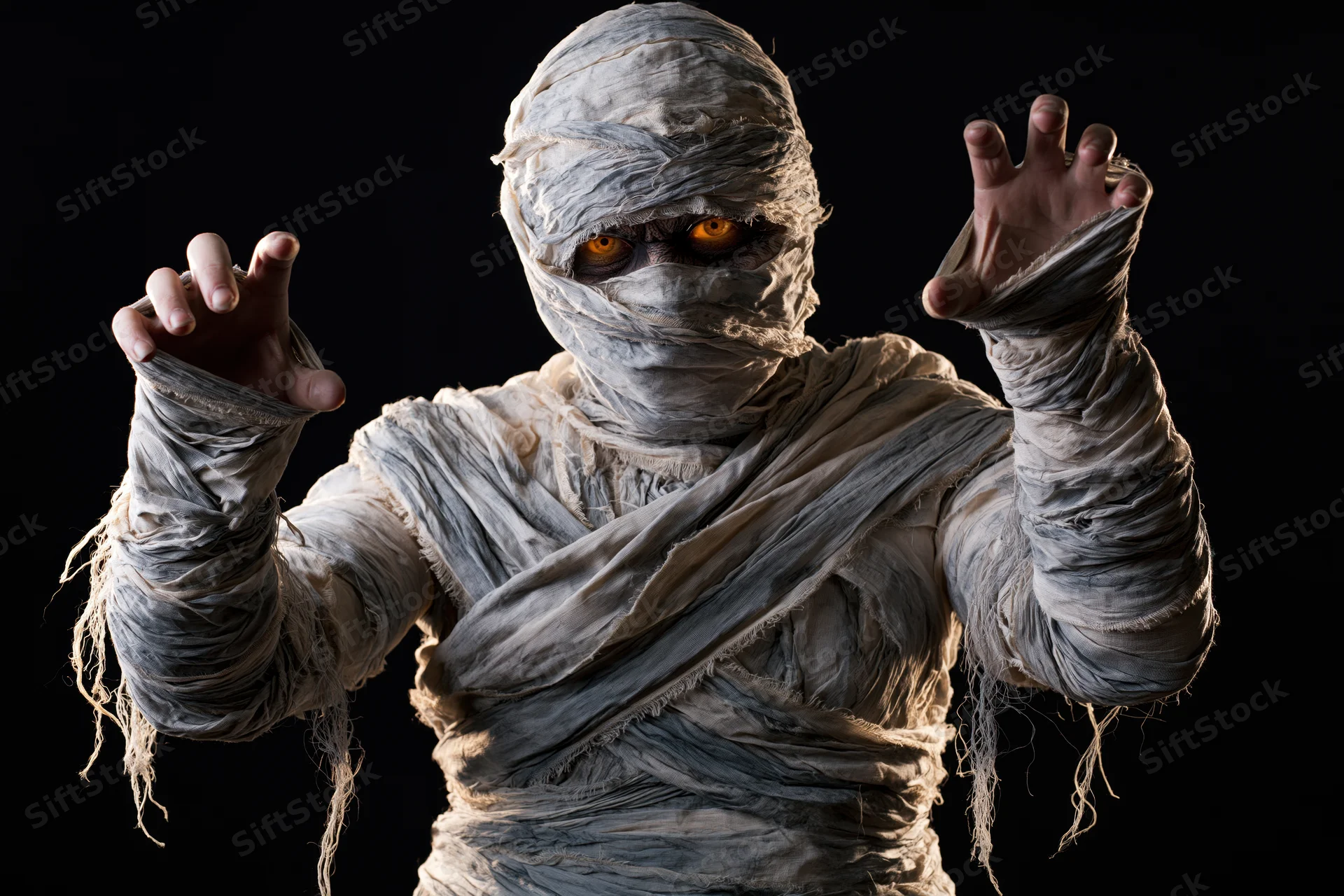 Mummy in full bandage costume posing with glowing eyes against black background