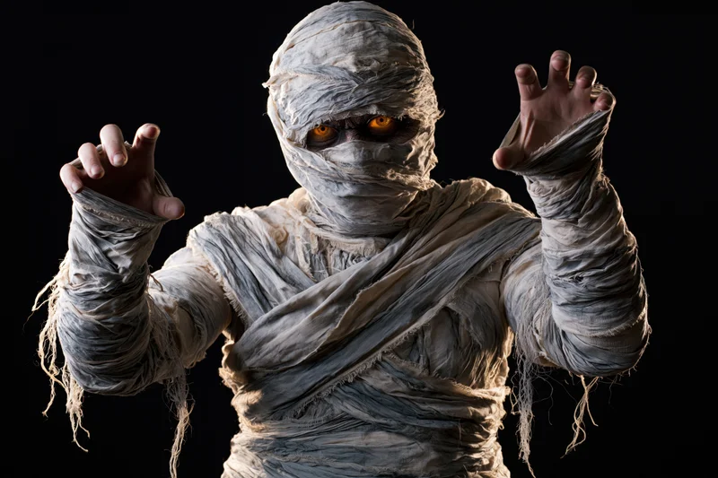 Mummy in full bandage costume posing with glowing eyes against black background