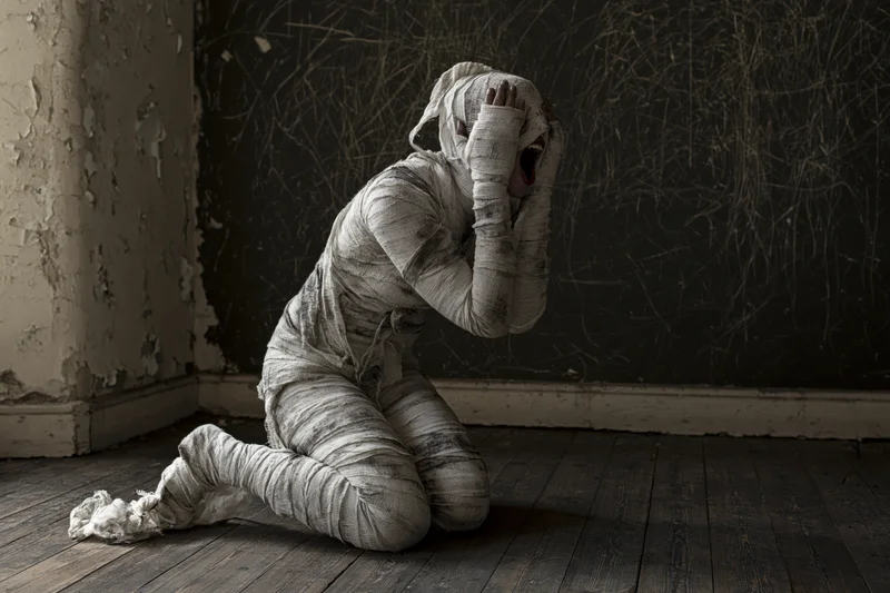Mummy wrapped in dirty bandages kneeling and screaming in a dark, decaying room