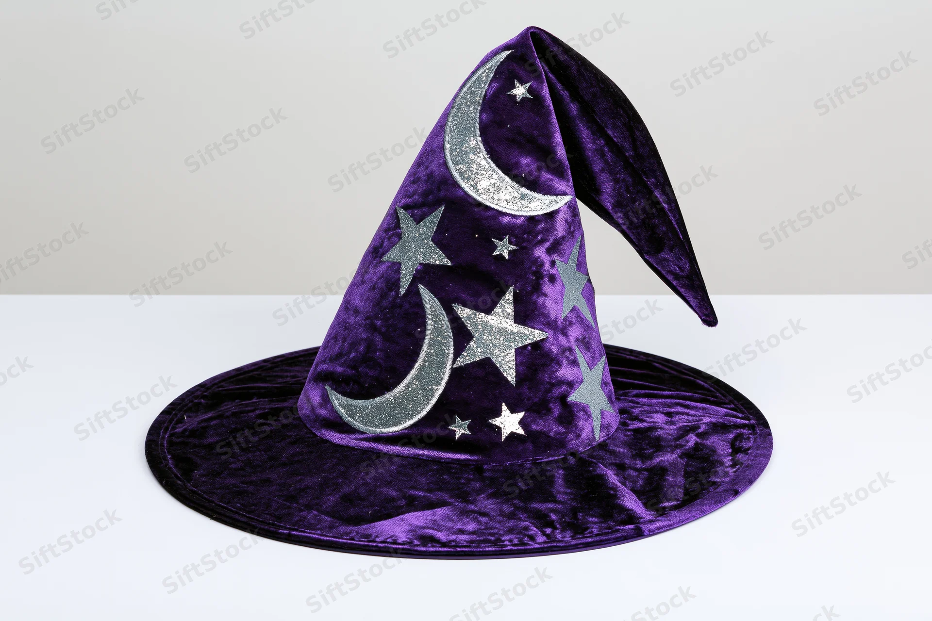 Purple velvet wizard hat with silver glitter moons and stars on white surface