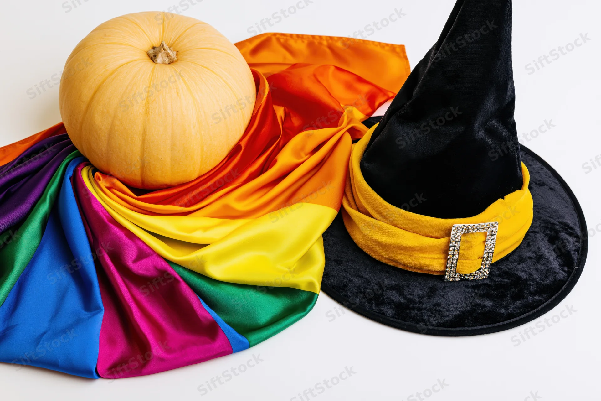Rainbow pride flag draped with a pumpkin and witch hat on white surface