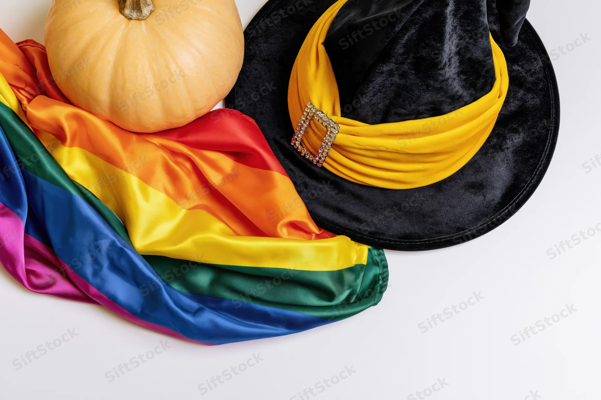 Rainbow pride flag with witch hat and pumpkin arranged on white surface