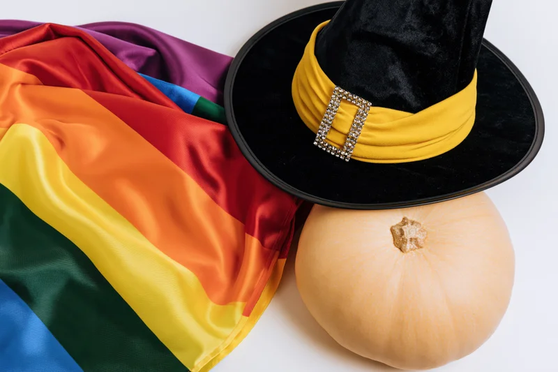 Rainbow pride flag fanned out beside a witch hat and pumpkin on white surface