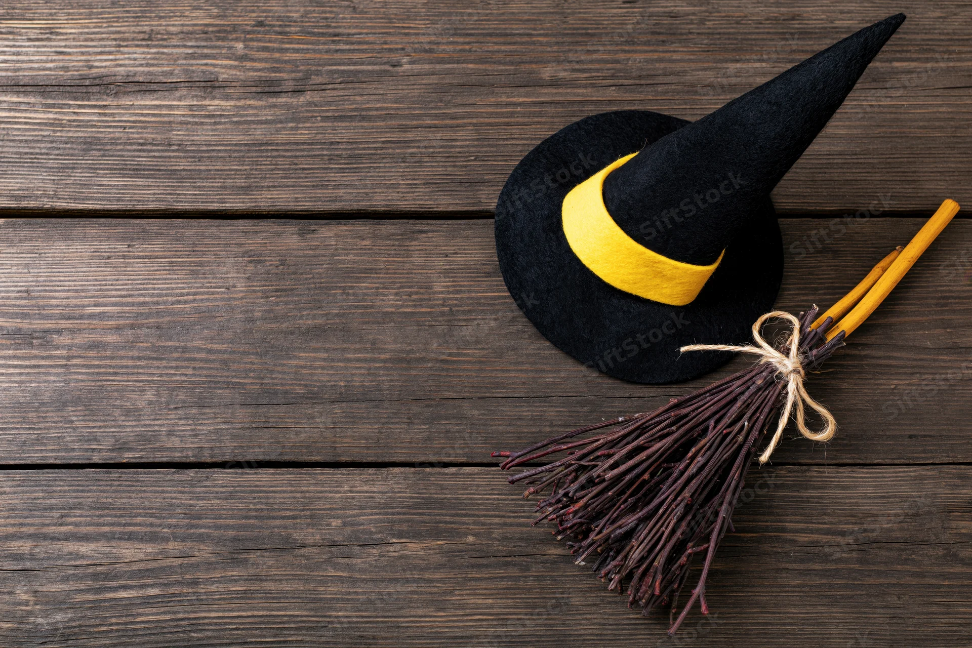 Black witch hat with yellow band and twig broom on wooden surface