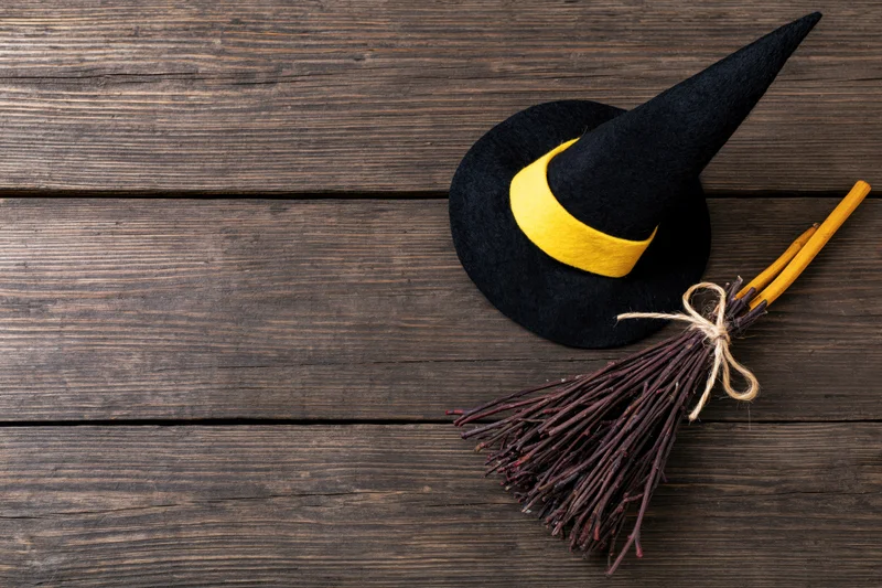 Black witch hat with yellow band and twig broom on wooden surface