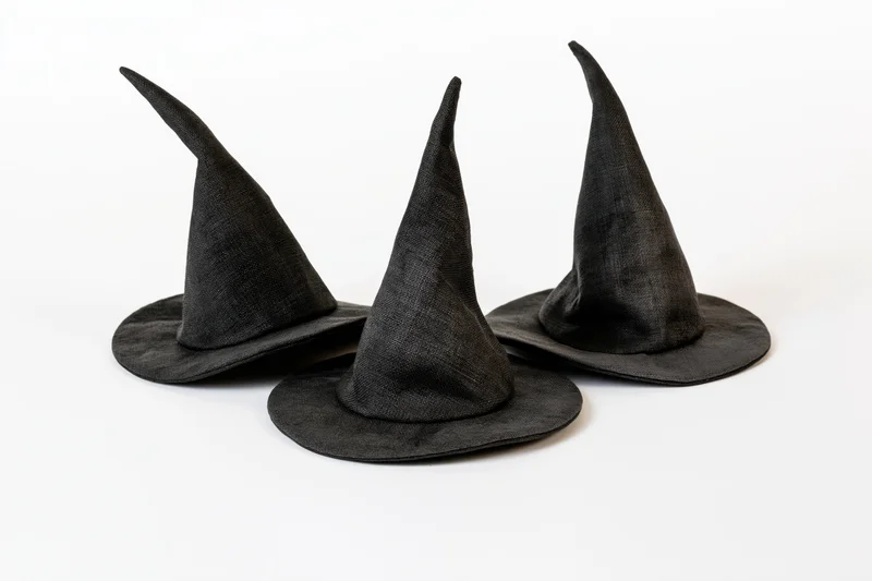 Three small black fabric witch hats arranged in a loose cluster on a white background