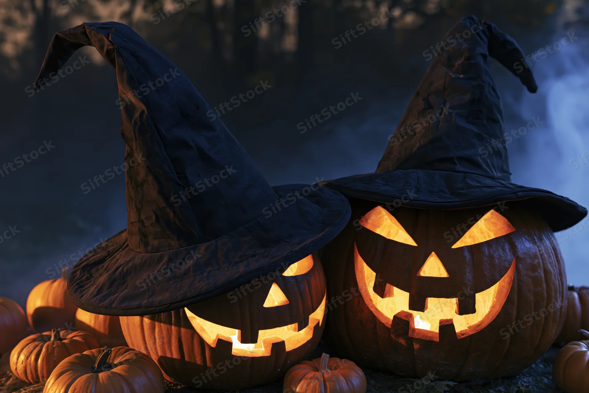 Two carved jack-o-lanterns wearing black witch hats glowing in a misty forest at night
