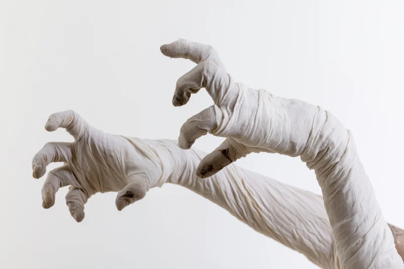 Two hands wrapped in aged white medical gauze bandages reaching forward against a plain background