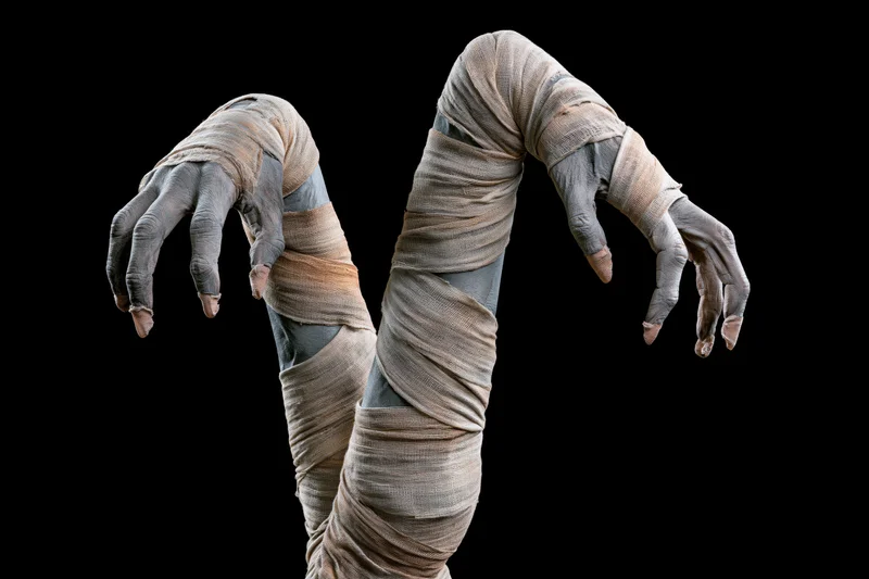 Mummy hands wrapped in bandages reaching forward against black background