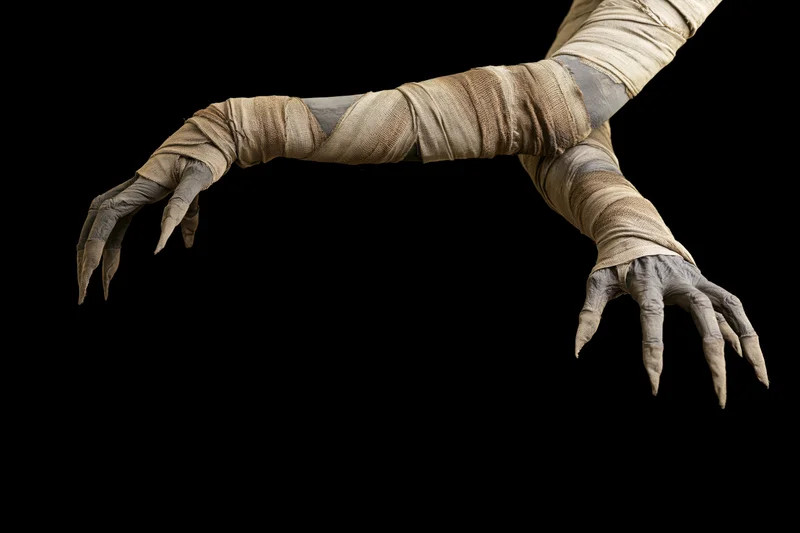 Mummy hands wrapped in bandages reaching forward against black background