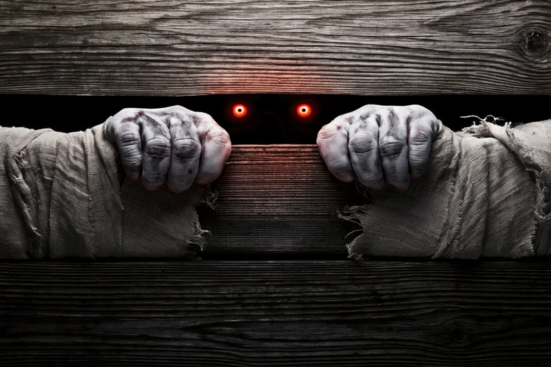 Mummy hands gripping wooden edge with glowing red eyes visible behind