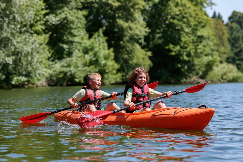 Two children paddling together in an orange tandem kayak on a calm river surrounded by green trees