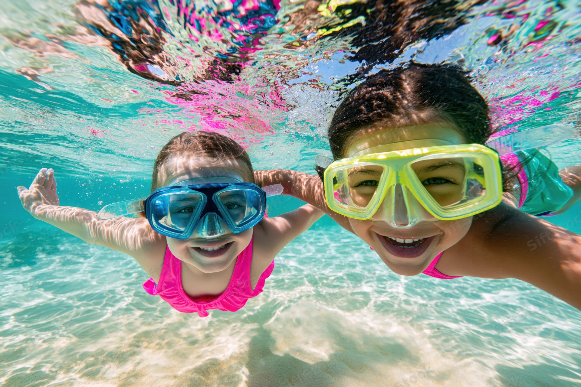 Two young girls smiling while snorkeling underwater in shallow tropical sea