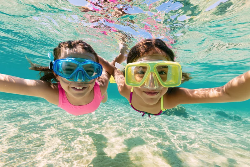 Two young girls swimming underwater in shallow tropical sea wearing snorkel masks and smiling