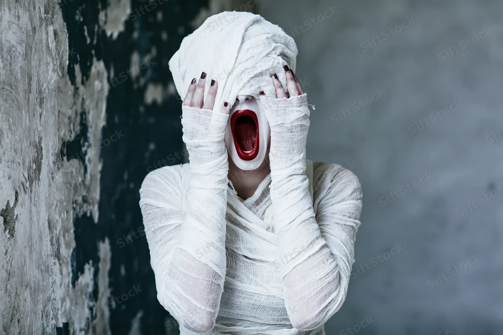 Woman in halloween mummy costume screaming with mouth wide open against grunge wall