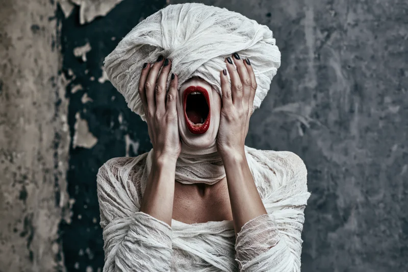 Woman in mummy costume screaming with hands on head against textured wall