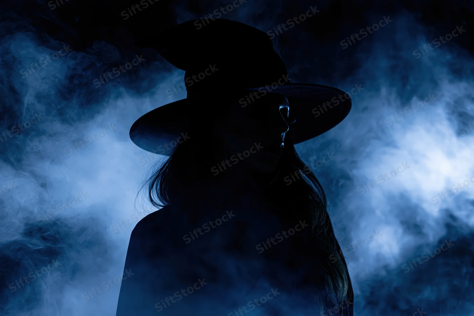 Woman in wide-brimmed witch hat as dark silhouette in blue smoke
