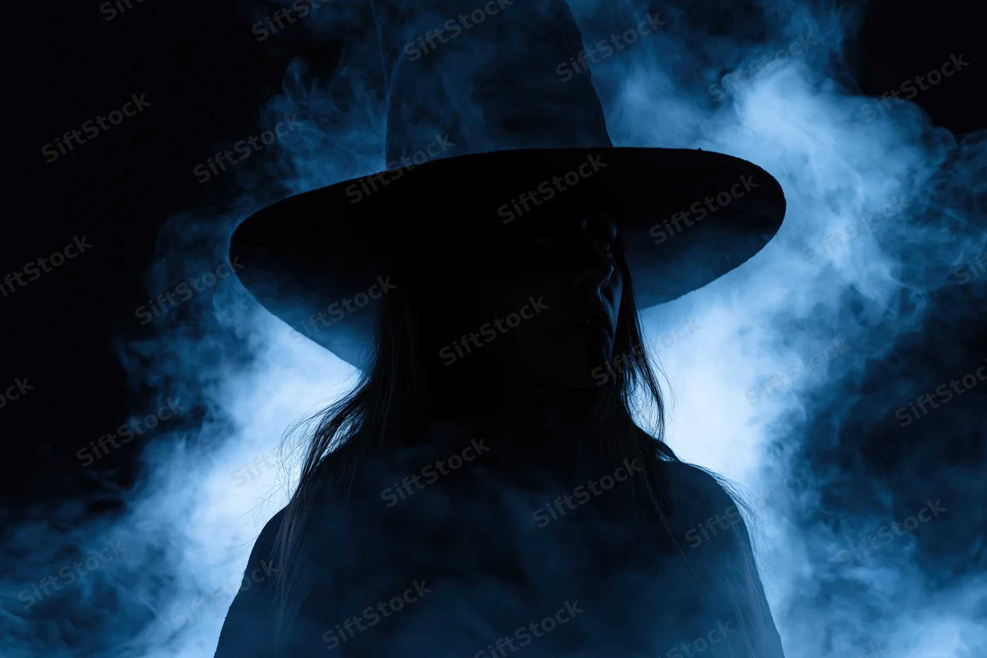 Woman in wide-brimmed witch hat as dark silhouette surrounded by blue smoke