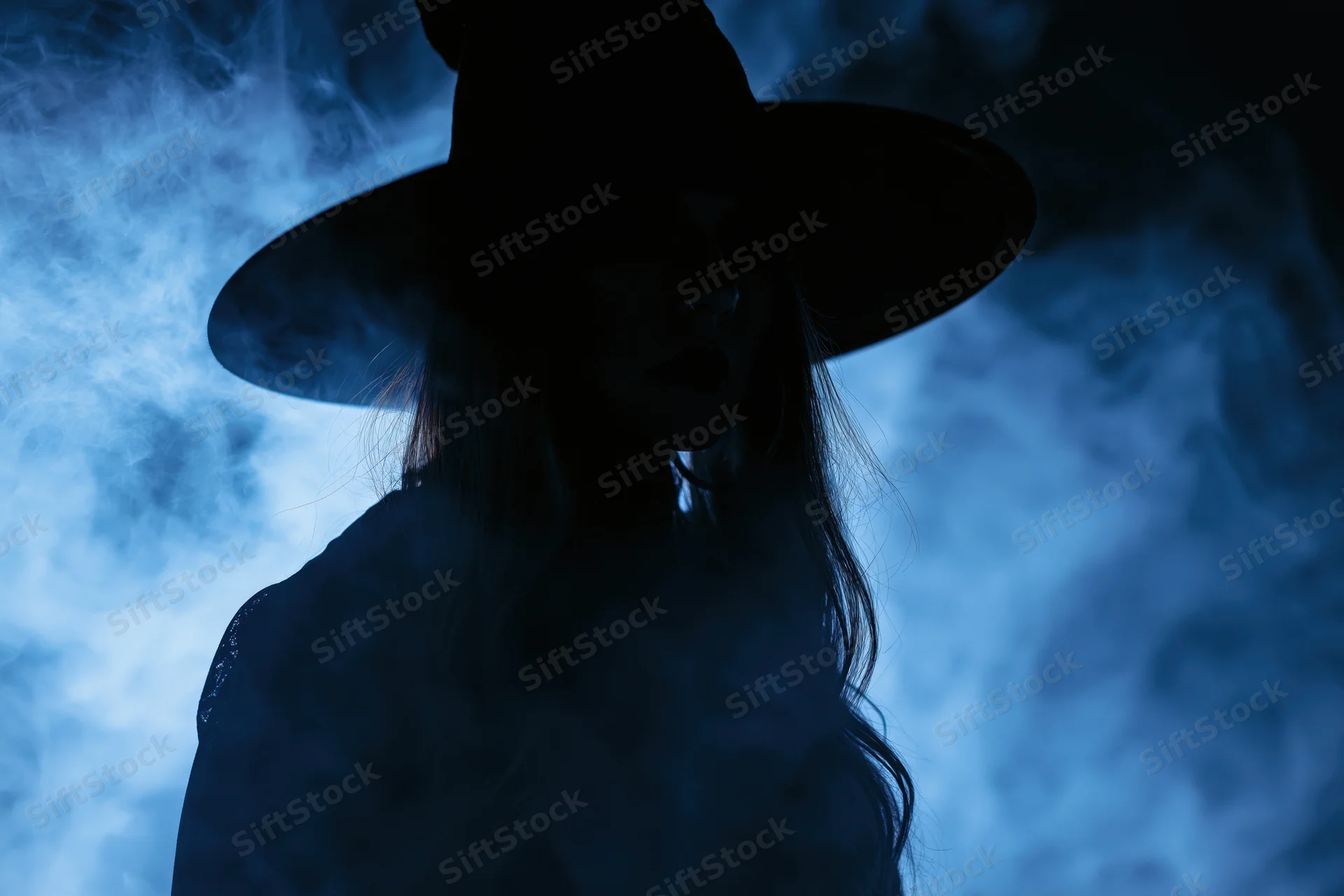 Woman in wide-brimmed witch hat as dark silhouette in blue smoke