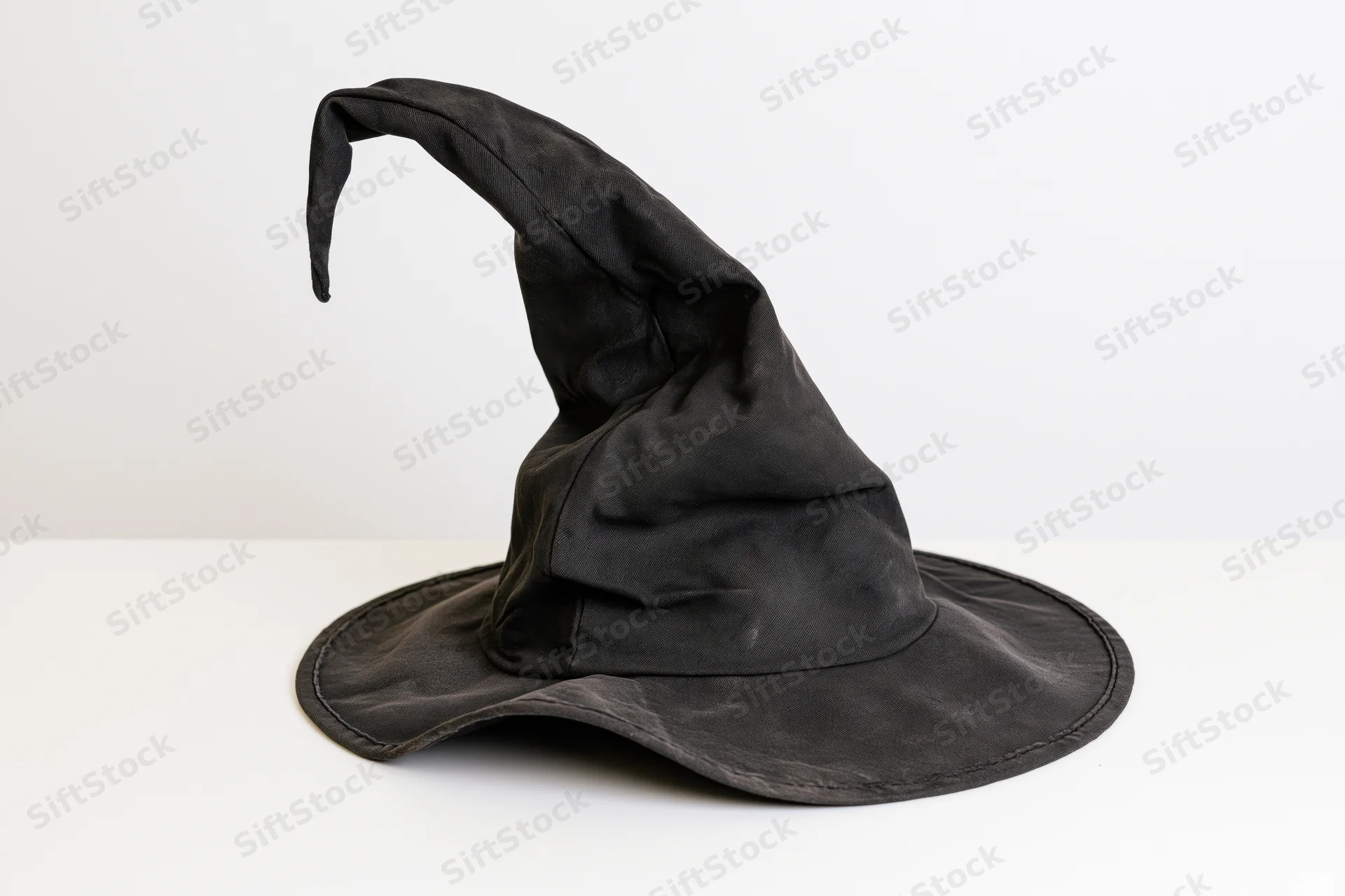 Worn black witch hat with crooked twisted tip on white surface