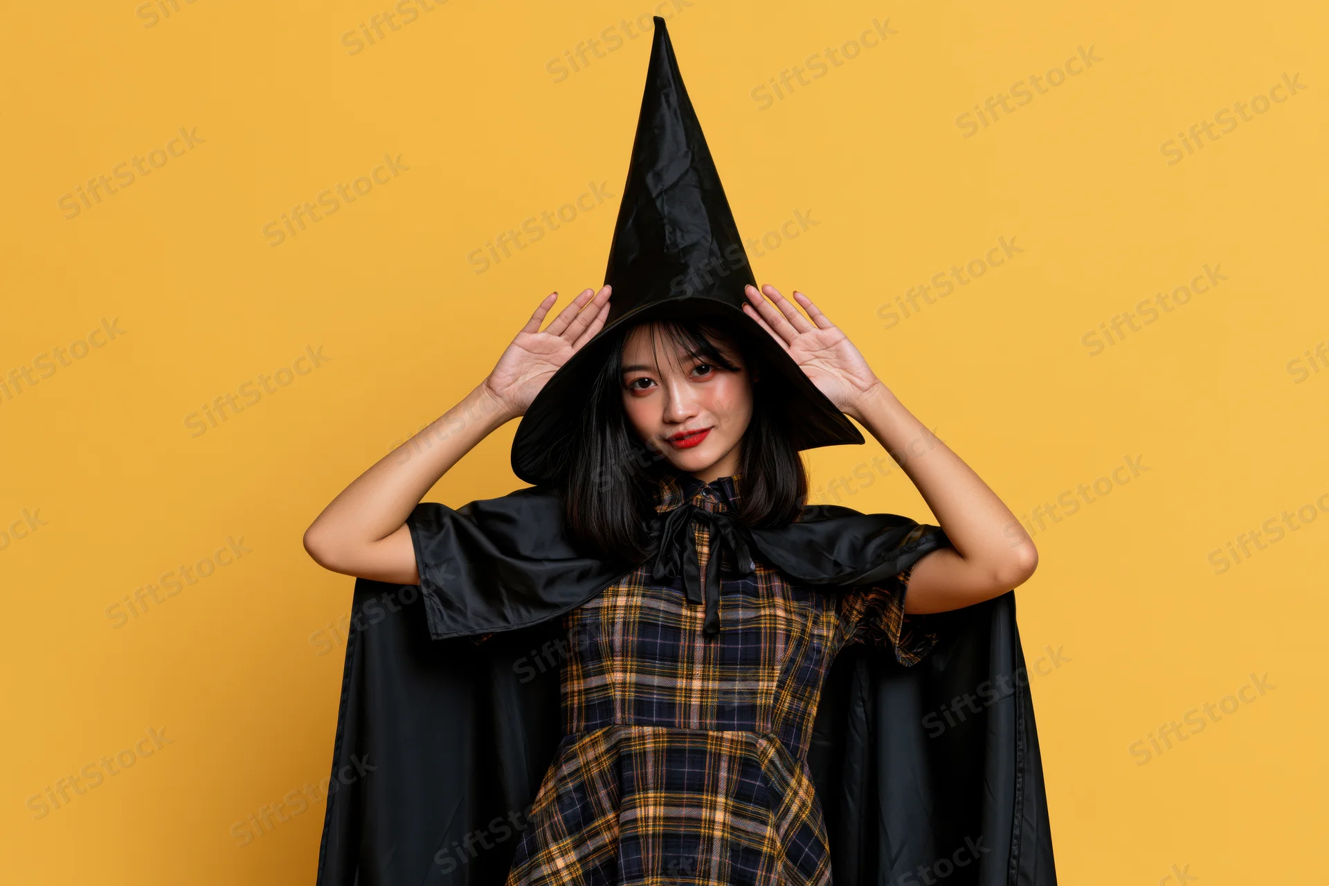 Young asian woman in witch costume posing playfully against yellow background