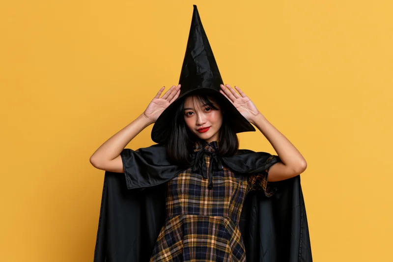 Young asian woman in witch costume posing playfully against yellow background