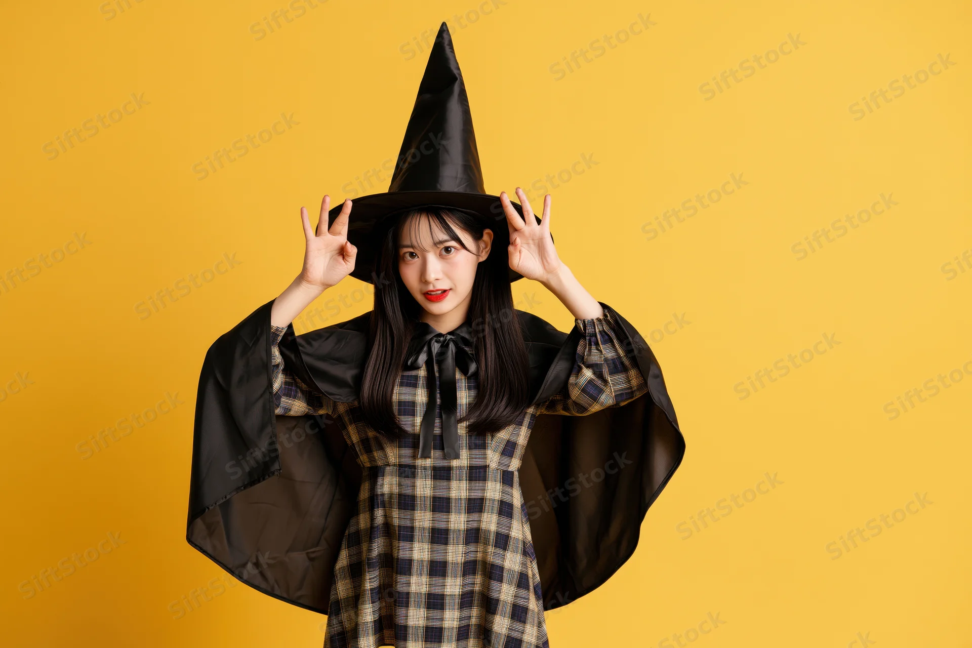 Young asian woman in witch costume posing playfully against yellow background