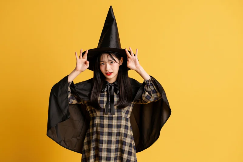 Young asian woman in witch costume posing playfully against yellow background